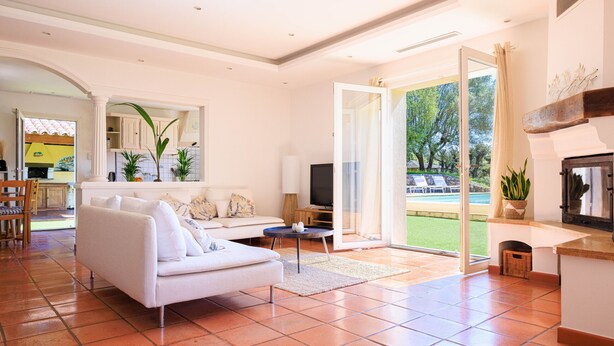 A spacious living room with a white sofa, a television, and a large window offering a view of the outdoors.