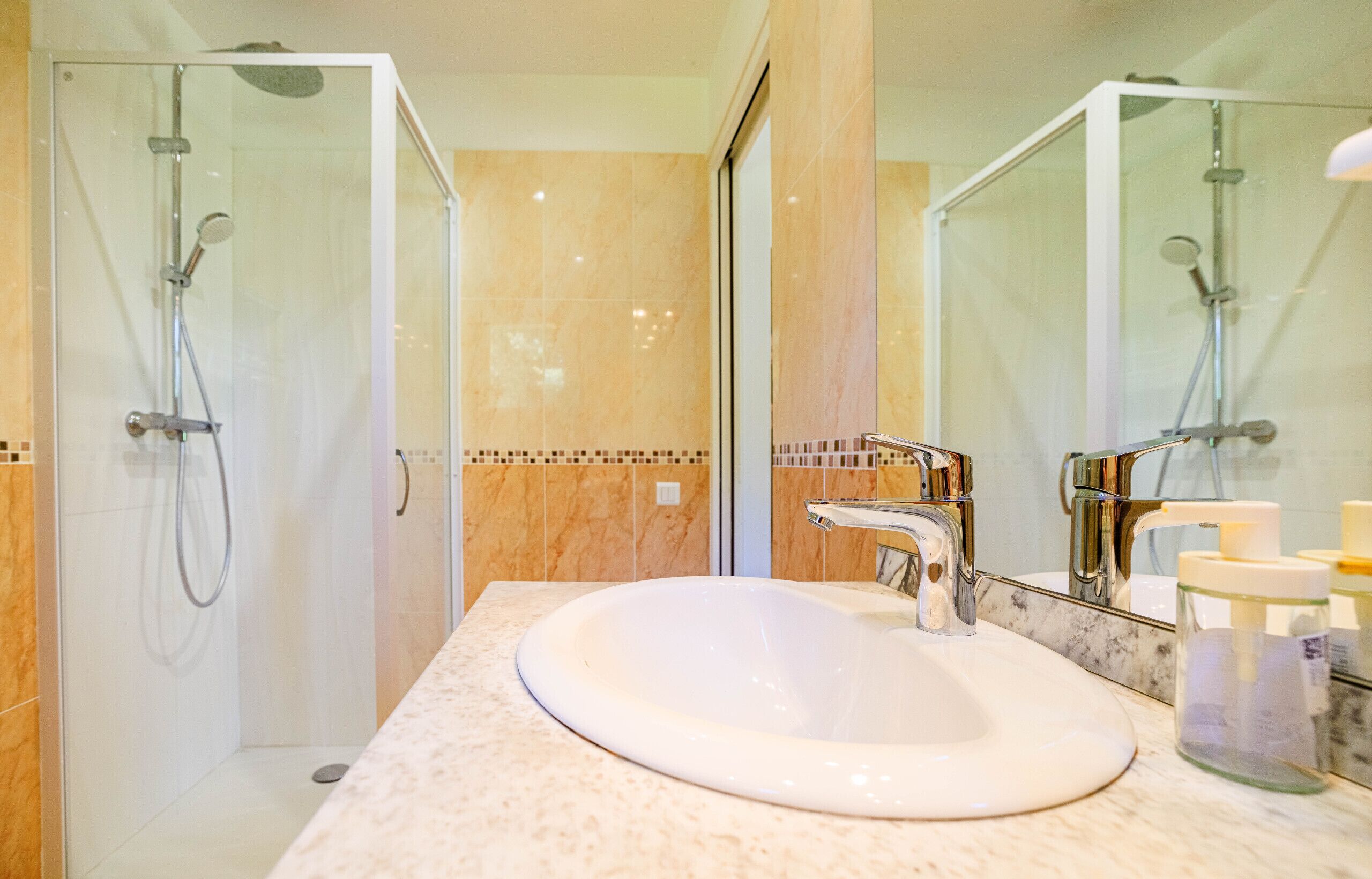 A modern bathroom with a glass-enclosed shower, a white sink, and a large mirror.
