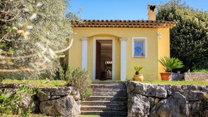 A yellow building with a tiled roof, a stone staircase leading to a door, and potted plants around.