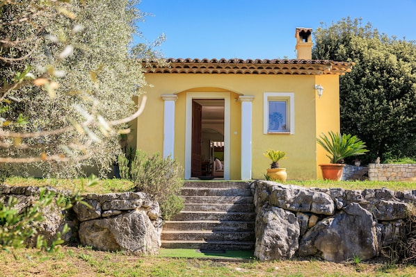 A yellow building with a tiled roof, a stone staircase leading to a door, and potted plants around.