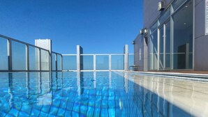 Ein klares, blaues Schwimmbecken mit Glasbarriere und ein modernes Gebäude mit großen Fenstern im Hintergrund.