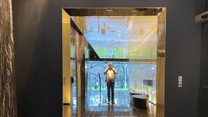 Eine Person steht in einer modernen Lobby, deren Glaswand das Innere reflektiert.