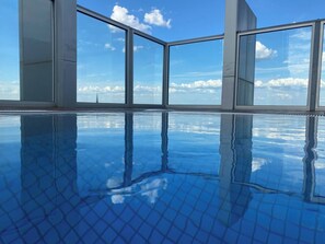 Ein klarer Innenpool mit Glasdecke, der Himmel und Wolken spiegelt.