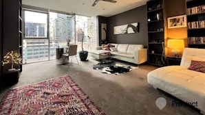 Ein modernes Wohnzimmer mit großem Fenster, einem weißen Sofa, einem schwarz-weißen Teppich, einem Deckenventilator und einem Bücherregal.