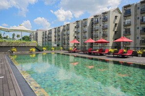 A swimming pool with clear water, surrounded by red lounge chairs and umbrellas, with a backdrop of multi-story residential buildings. - Family-friendly 3BR Apartment in Serene Malabe (Kolonnawa)