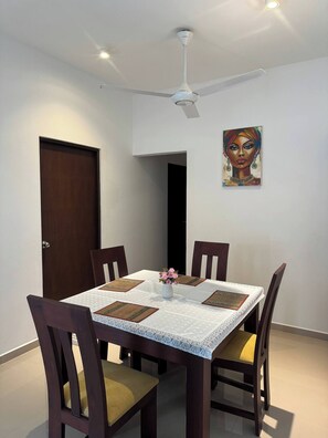 A dining area with a table set for four, surrounded by wooden chairs with cushioned seats. A ceiling fan is mounted above the table, and a painting is visible on the wall. - Family-friendly 3BR Apartment in Serene Malabe (Kolonnawa)