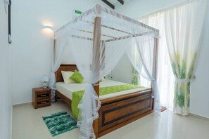 Un dormitorio con una cama de madera, ropa de cama verde, una mesita de noche, una alfombra verde y cortinas translúcidas.
