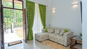 Ein Wohnzimmer mit einem Ecksofa, einem Glastisch und Blick auf Grünfläche draußen.