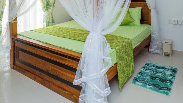 Ein Schlafzimmer mit einem hölzernen Bett, grüner Bettwäsche, einem weißen Moskitonetz und einem grünen Teppich.
