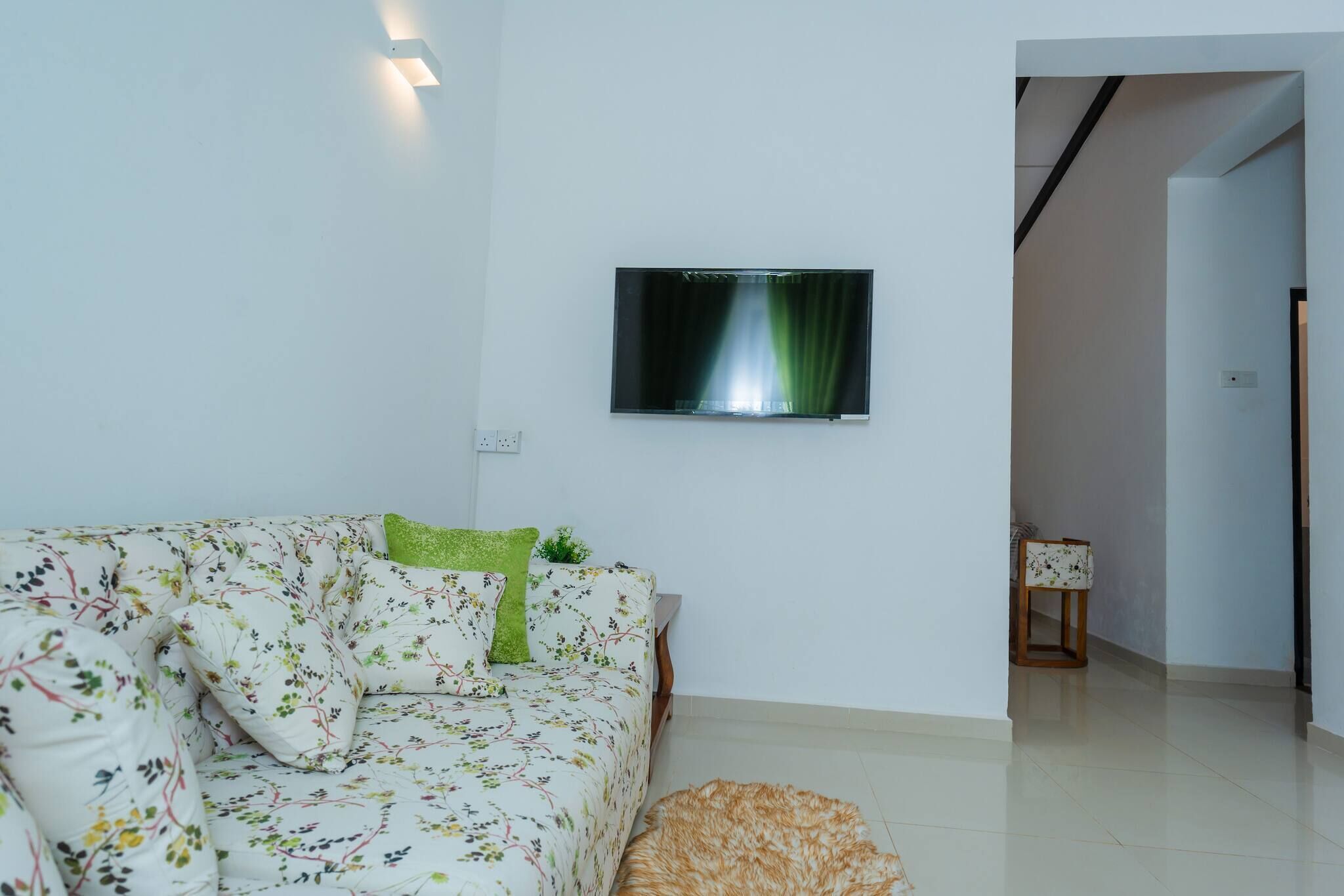 A living room with a sofa, a television mounted on the wall, and a small table with a lamp.