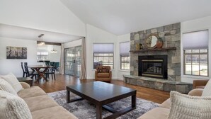 A spacious living room with a stone fireplace, a dining area with a glass door, and a large window.