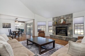 A spacious living room with a stone fireplace, a dining area with a glass door, and a large window.