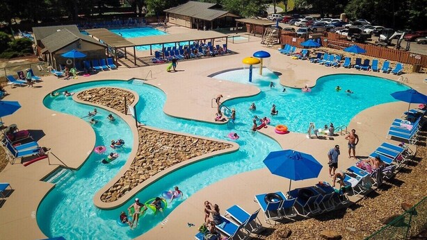 A swimming pool area with multiple pools, lounge chairs, and umbrellas.