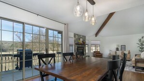 A spacious dining area with a large wooden table and chairs, a fireplace, and a view through large sliding glass doors to an outdoor deck.
