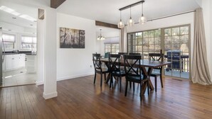 A spacious dining area with a wooden table and chairs, a large window with a view, and a modern kitchen in the background.