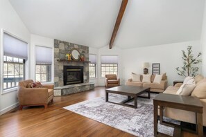 A spacious living room with a stone fireplace, wooden flooring, and a large window.