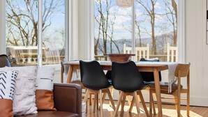 En moderne stue med et stort vindue, et spisebord med stole og en hængende lampe.