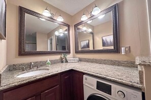 Une salle de bain avec deux grands miroirs, un lavabo, un lave-linge et un porte-serviettes.