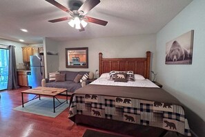 A bedroom with a bed, a ceiling fan, a wooden headboard, a sofa, and a dining table.
