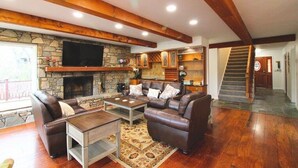 A living room with a stone fireplace, leather sofas, a coffee table, and a staircase.