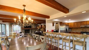 A spacious kitchen with wooden beams, a chandelier, and a stone fireplace.