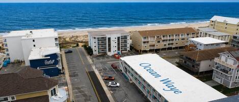 A coastal hotel with a prominent 'Ocean Way' sign, a parking lot, and a view of the beach and ocean.