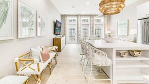 Une cuisine moderne avec des meubles blancs, un îlot central et un coin repas comprenant des chaises et un banc, le tout dans des tons blancs.