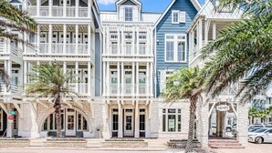 Une rangée d’immeubles à plusieurs étages dotés de balcons, une enseigne indiquant « Tiki-Jays », et des palmiers au premier plan.