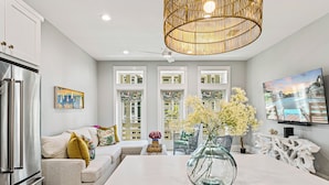 A modern kitchen with a large island, a dining area with a white table, and a living room with a sofa and decorative items.
