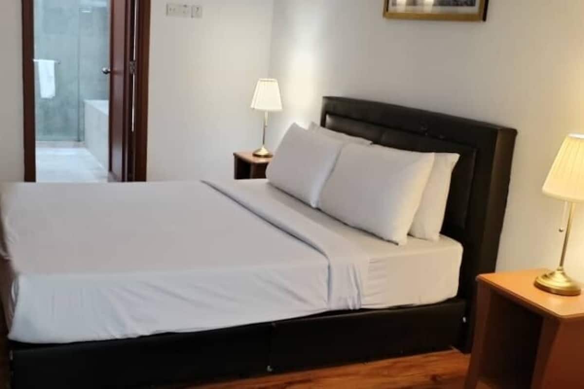 A hotel room with a bed, two bedside lamps, a wooden floor, and a door leading to a bathroom.