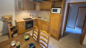 A kitchen with wooden cabinets, a microwave, a stove, and a dining area with chairs and a table. - LE MAZET DE LA REGORDANE (Saint-André-Capcèze)