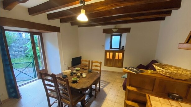A dining area with a wooden table and chairs, a small kitchen area with a window, and a door leading outside. - LE MAZET DE LA REGORDANE (Saint-André-Capcèze)