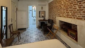 A hotel room with a fireplace, a desk with a chair, a bed, and a patterned floor. - Vasiliki Konak (Bozcaada)
