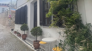 A building with a white facade, dark wooden shutters, and a balcony with potted plants. - Vasiliki Konak (Bozcaada)
