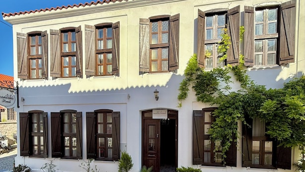 A two-story building with multiple windows, a door, and potted plants. - Vasiliki Konak (Bozcaada)