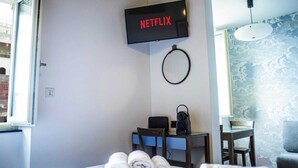 A hotel room with a bed, a desk, a chair, a TV mounted on the wall, and a window.