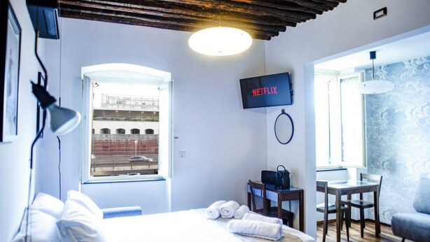 A hotel room with a bed, a desk, a chair, a TV, and a window with a view of a building.