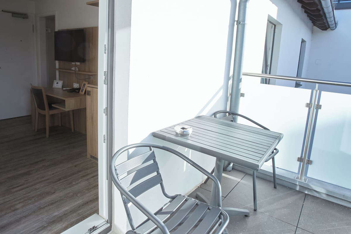 A balcony with a metal table and chairs, a TV mounted on the wall, and a wooden desk with a chair.