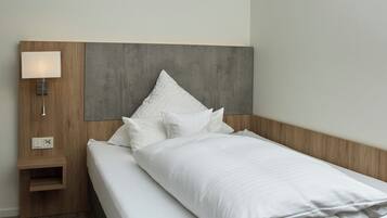Una habitación de hotel moderna con una cama bien hecha, una mesita de noche de madera con lámpara y un cabecero gris.