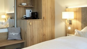 Ett hotellrum med en garderob i trä, en säng med vita sängkläder, ett nattduksbord med en lampa och en liten hylla med toalettartiklar.