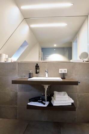 A modern bathroom with a skylight, a large mirror, and a wooden shelf with towels. - City Hotel Bocholt  (Bocholt)