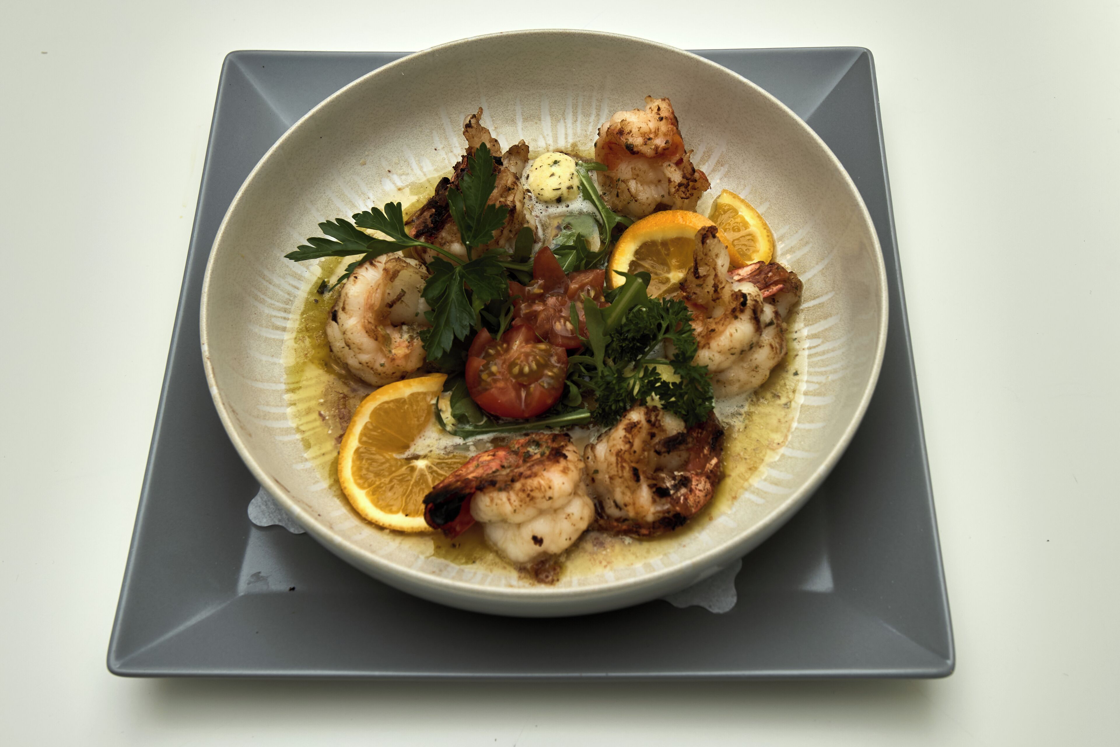 A plate of food with shrimp, lemon, and herbs.