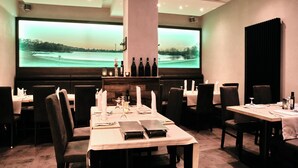 En restaurang med en stor skärm som visar en vacker utsikt, bord täckta med vita dukar och ett urval av flaskor på en hylla.
