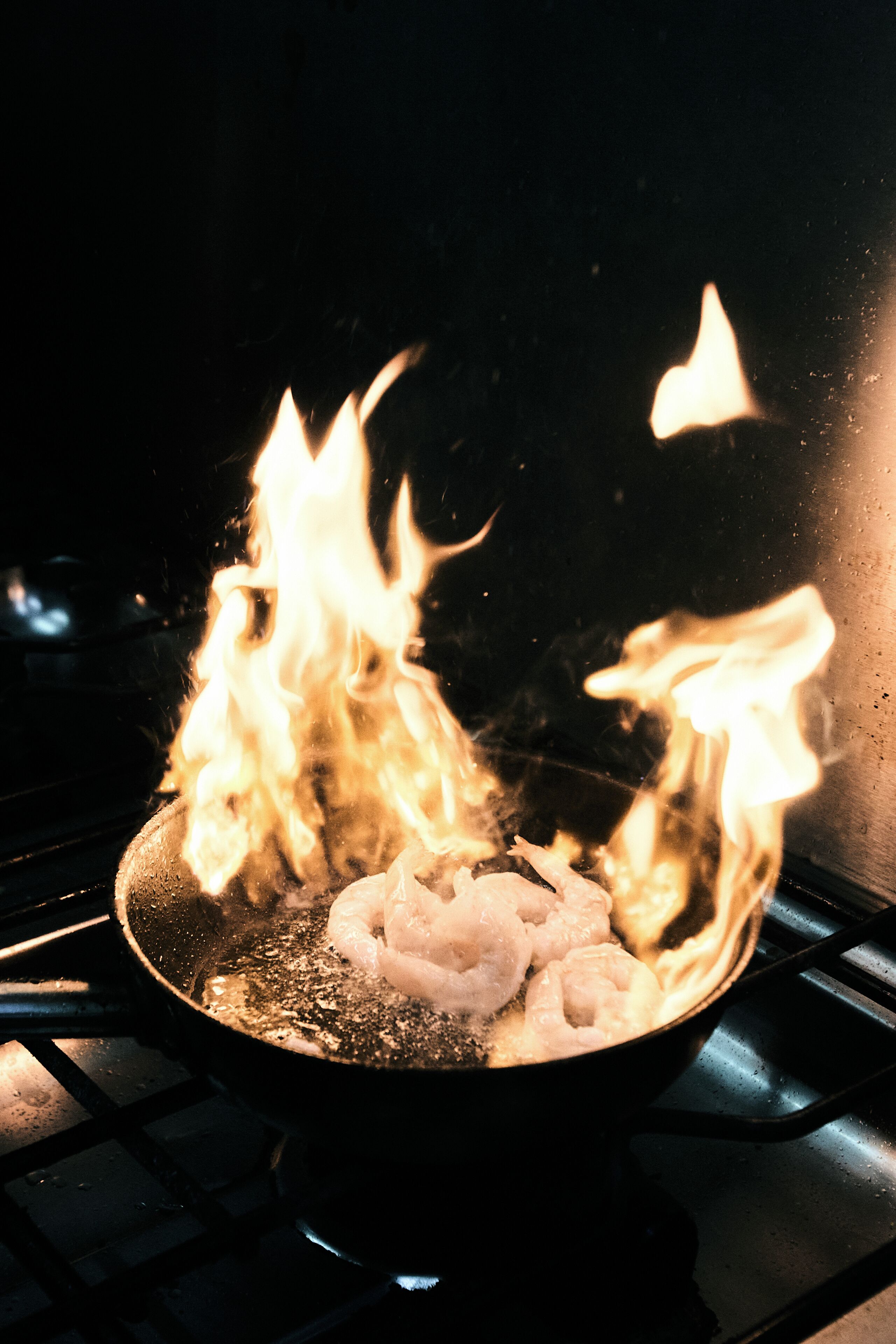 Eine Pfanne auf einem Herd mit Flammen und darin garenden Garnelen.