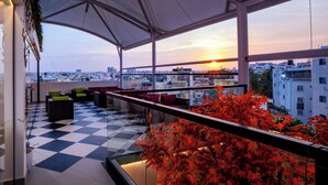 A rooftop terrace with a checkered floor, seating area, and a view of the sunset over the cityscape. - Hotel Paramos Meeds (Bengaluru)