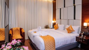 A modern hotel room with a large bed, a wooden floor, a seating area with a chair, and a potted plant. - Hotel Paramos Meeds (Bengaluru)