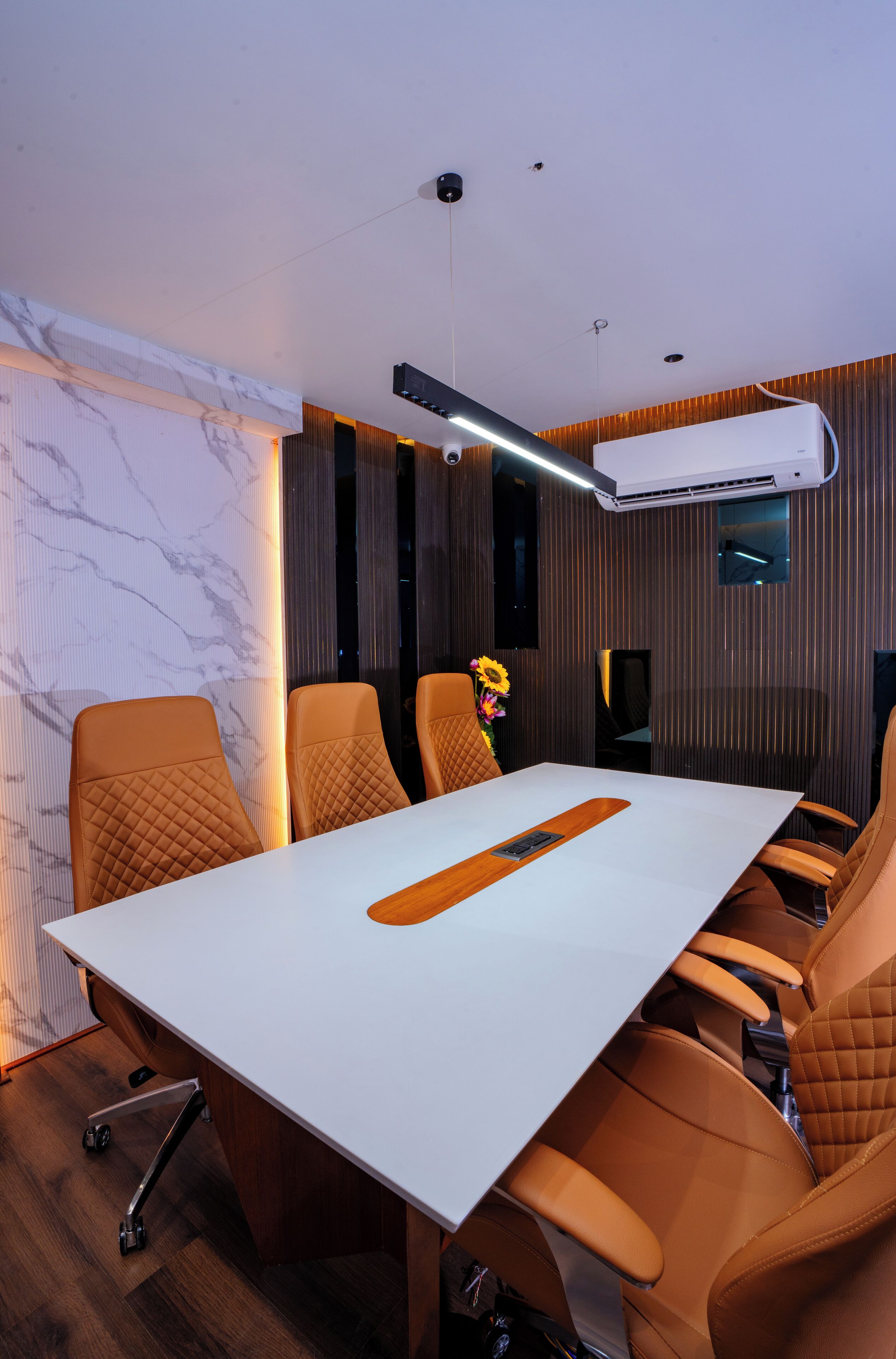 A conference room with a white table, brown leather chairs, a flower vase, and an air conditioning unit on the wall.