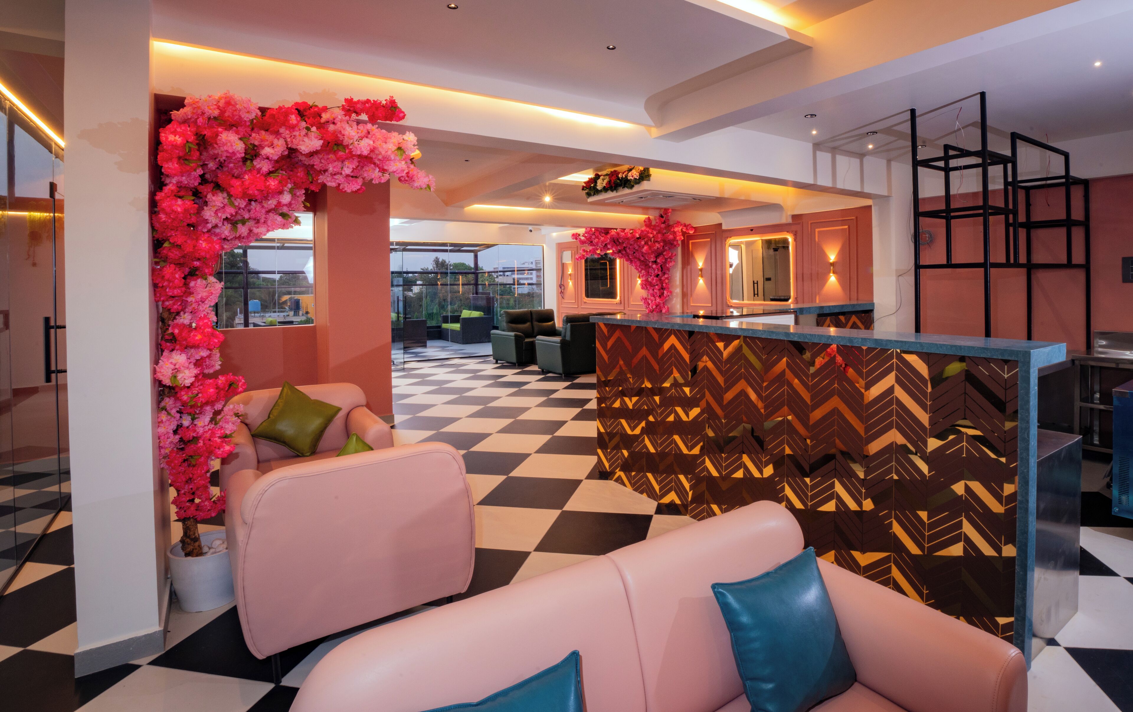A modern lobby with a checkered floor, pink and green sofas, a decorative floral arch, and a staircase with a black metal frame.