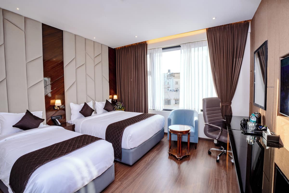 A hotel room with two beds, a desk, a chair, and a TV.