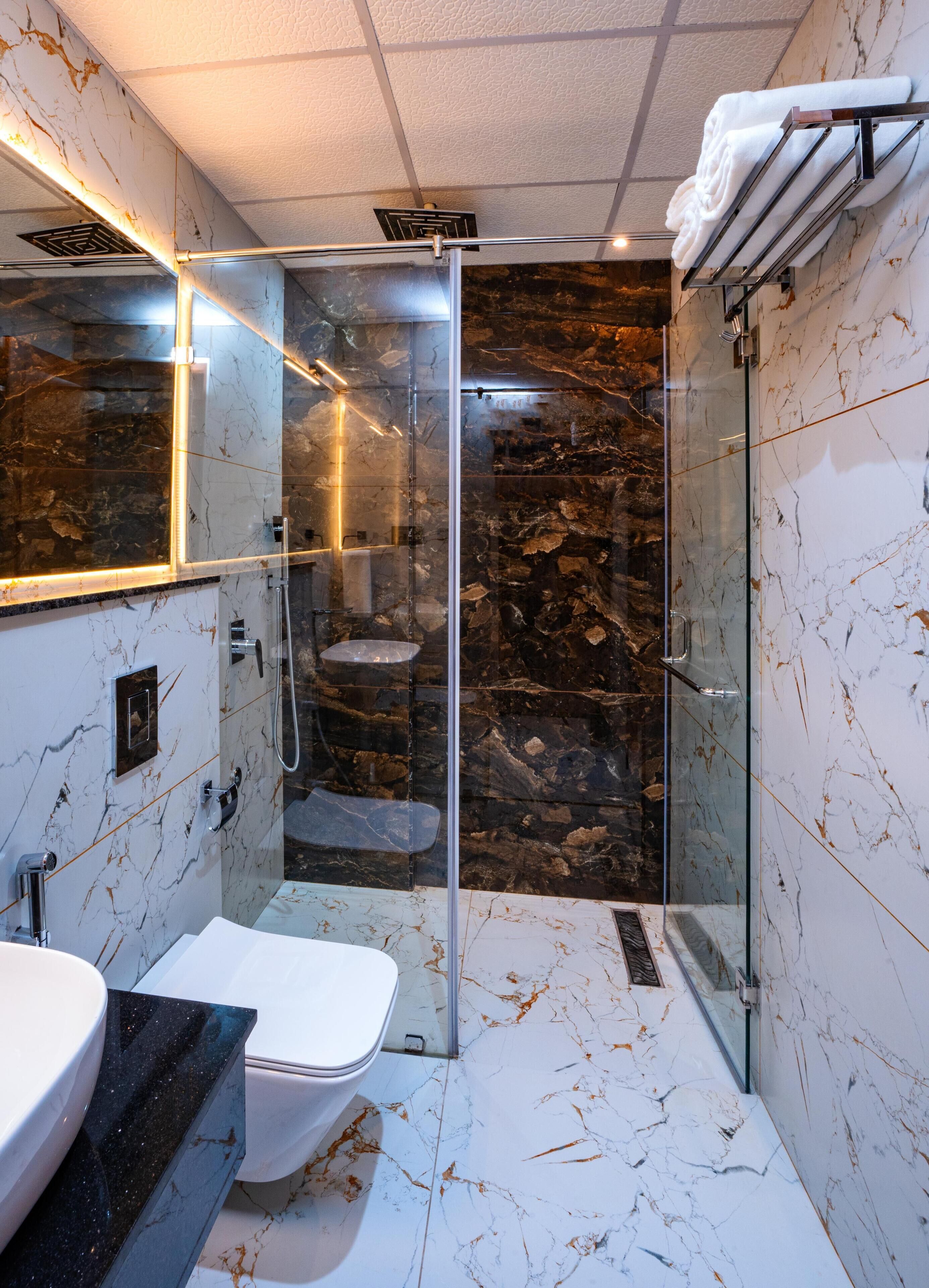 Un baño moderno con ducha de vidrio, paredes de mármol y un inodoro blanco.